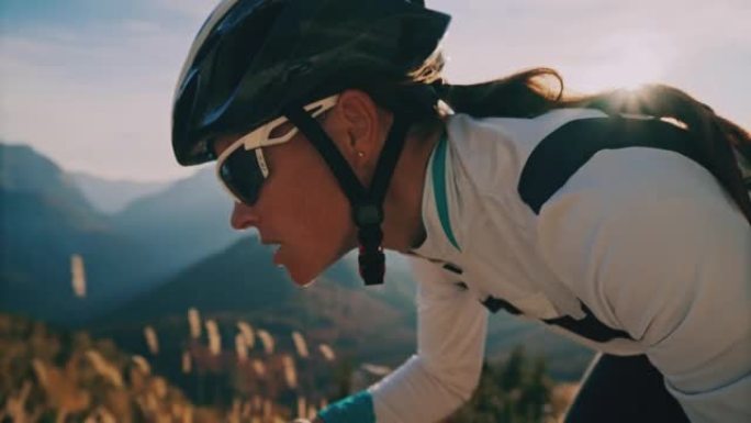 女骑车人在阳光明媚的风景秀丽的山区骑自行车上坡