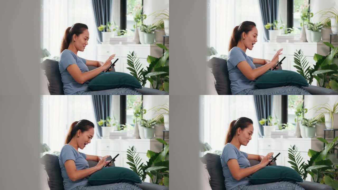 年轻的亚洲女性穿休闲网站在沙发上使用智能手机感觉令人兴奋的滚动屏幕在线购物在客厅室内植物在家里。