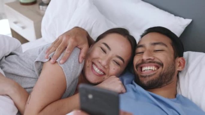 有趣的电话社交媒体，一对夫妇躺在卧室里，在网上看一个模因或笑话。已婚男女使用wifi和无线技术在线浏
