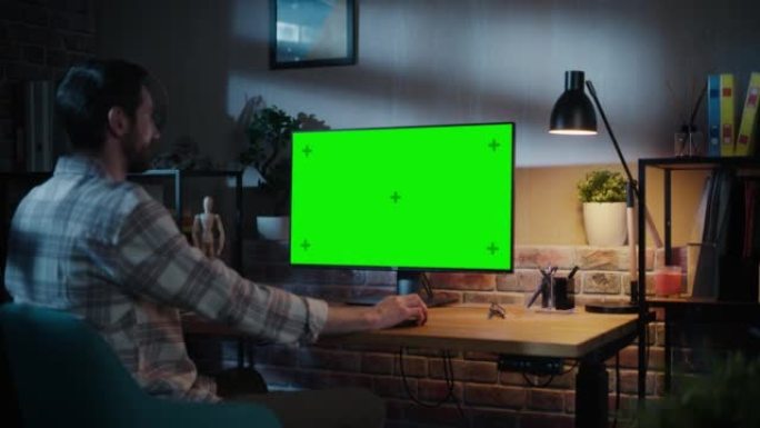 年轻有魅力的人在家用绿屏模拟显示的台式电脑工作。男性检查公司账户，给同事发信息。晚上阁楼客厅。放大镜
