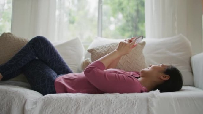 女人躺在家里的沙发上使用智能手机