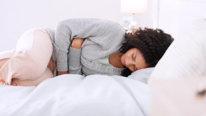 月经，月经和抽筋，一个女人躺在床上，在家里的卧室里痛苦地抱着肚子。肚子抽筋的年轻女性在屋子里的房间里