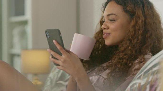 4k视频片段，一名年轻女子使用智能手机并在家中床上喝咖啡