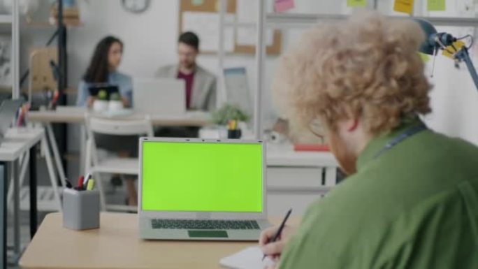 现代办公室中员工看着绿色色度键笔记本电脑屏幕的后视图