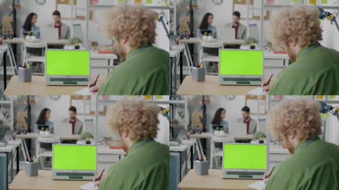 现代办公室中员工看着绿色色度键笔记本电脑屏幕的后视图
