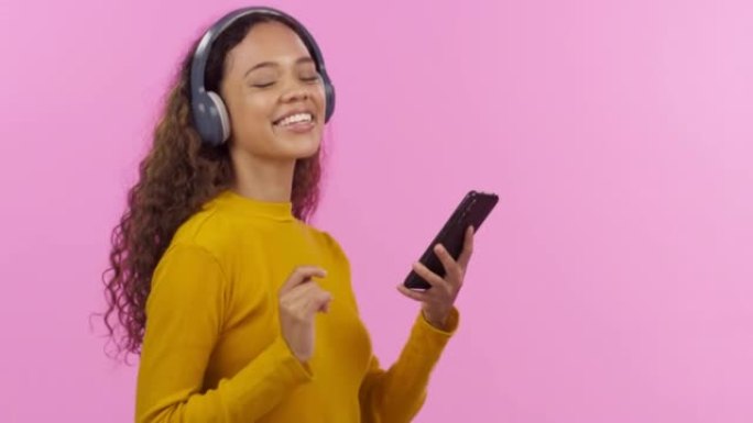 美丽的年轻混血女子一边用手机一边耳机听音乐。快乐混血模特儿随音乐跳舞戴耳机透过音乐浏览