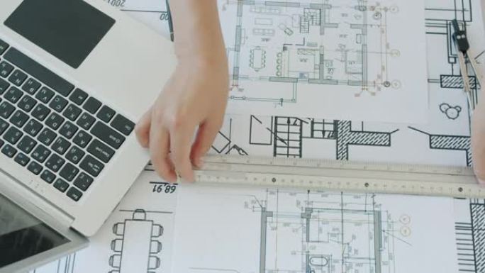 建筑师手的高角度视图绘制施工图和使用笔记本电脑打字