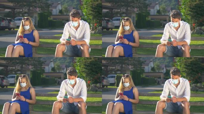 特写: 两个陌生人坐在公园长椅上发短信时戴着口罩。