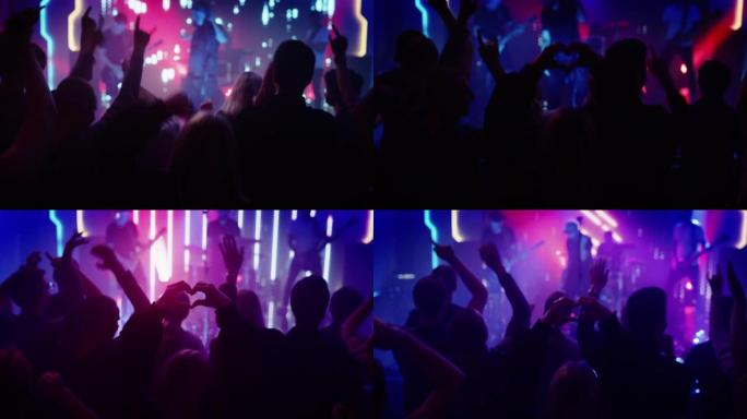人正在做一个心形手势，并在表演中举手。摇滚乐队在舞台上的夜总会音乐会上演奏一首歌，灯光鲜艳。