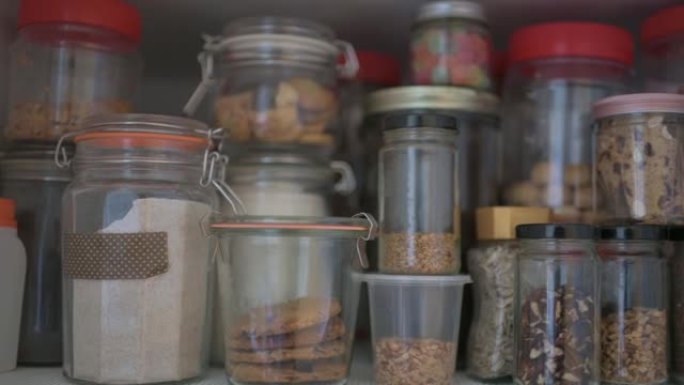 平移拍摄显示了厨房饼干，种子，生食，腌制食品，干食品和面粉在罐子和塑料容器中的货架橱柜中的食物存储