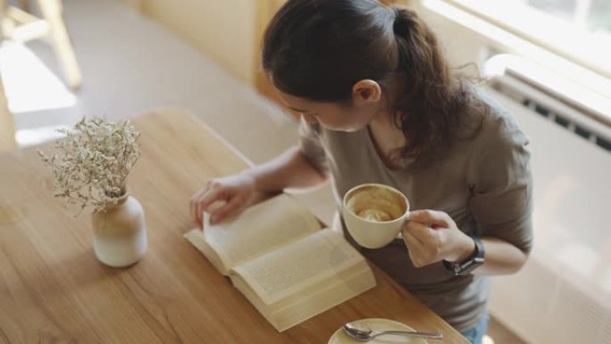 亚洲女人用咖啡杯看书，在日常生活活动中放松