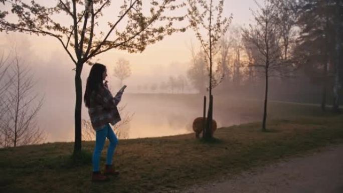 年轻女子在雾湖散步时使用手机