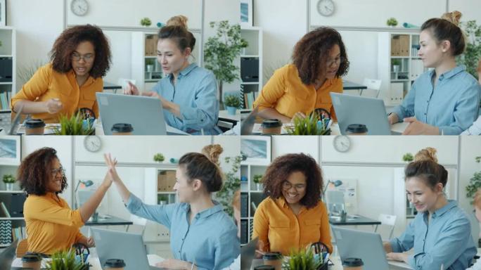 快乐的美国黑人和亚洲女孩在办公室里看着笔记本电脑屏幕说话的慢动作