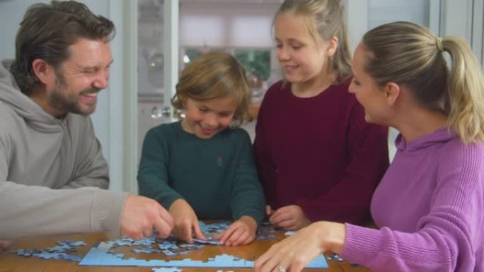 有孩子的家庭坐在家里的桌子旁一起做拼图游戏