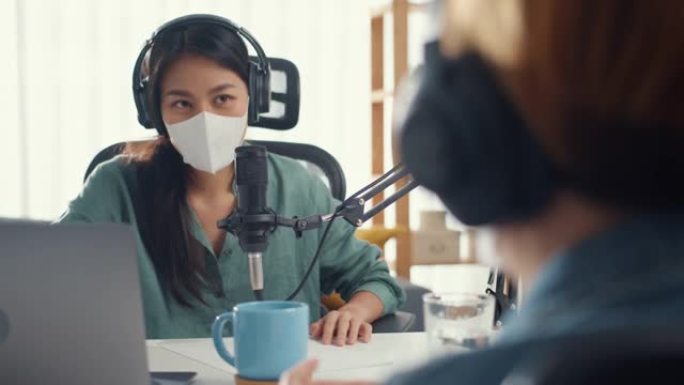 亚洲女孩电台主持人录音播客使用麦克风戴耳机采访嘉宾内容戴口罩保护病毒谈话在她的房间里听。