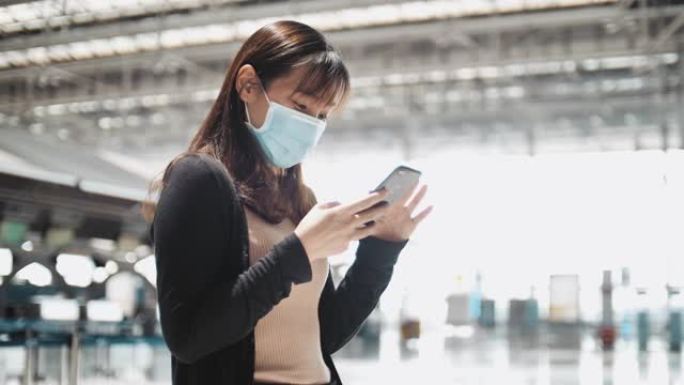 亚洲妇女在机场戴外科口罩检查智能手机上的登机牌