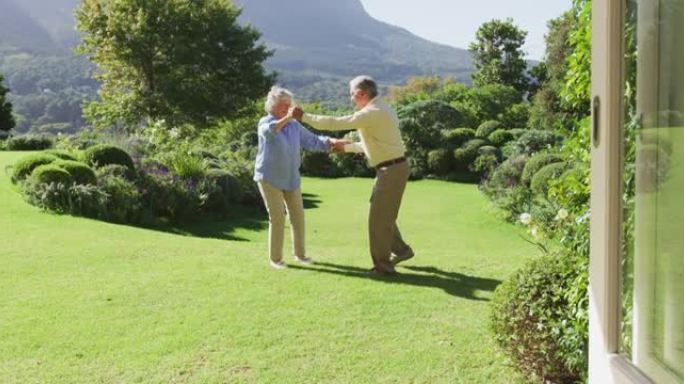 快乐的高加索高级夫妇在阳光明媚的日子里在花园里一起跳舞