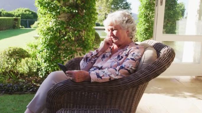 体贴的白人高级女性坐在户外的椅子上使用智能手机