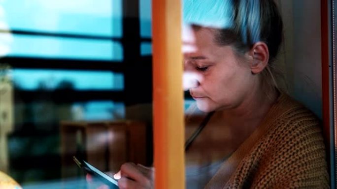 SLO MO悲伤的女人在在家订购期间坐在阳台门前的地板上时使用智能手机