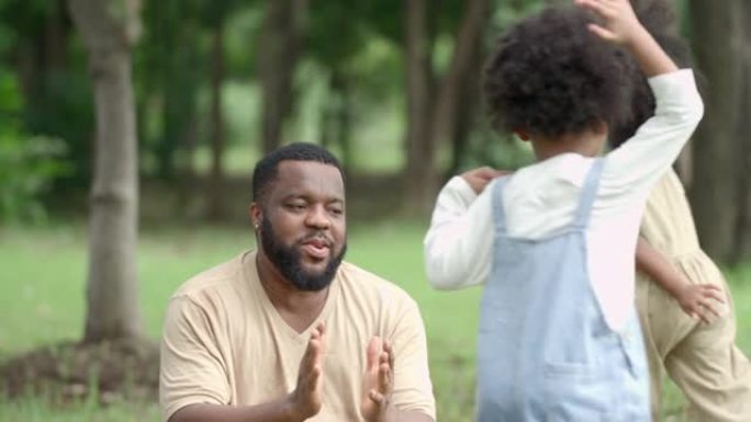 一个黑人女儿在她父亲周围的公园里玩耍。在一起度过的快乐时光中，每个人的脸上都充满了微笑。
