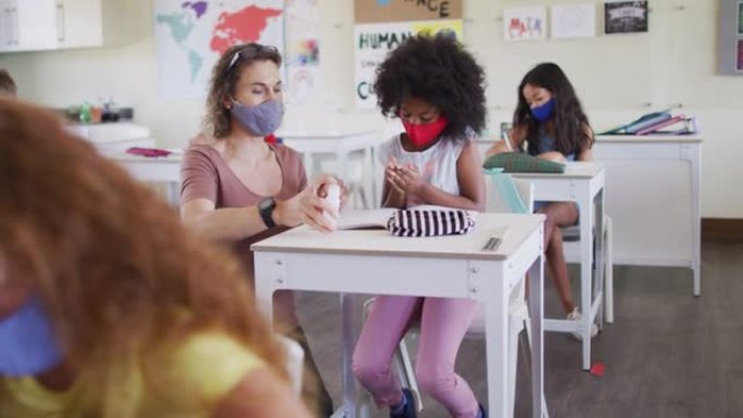 女教师和女孩戴着口罩在学校消毒双手
