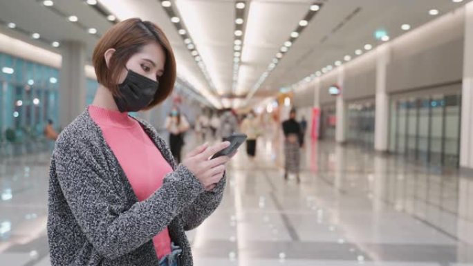 亚洲妇女戴口罩在机场使用智能手机