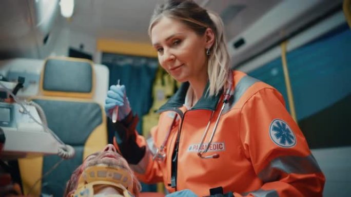 女性专业急救护理人员在救护车上与受伤病人一起前往医疗保健医院。她用手电筒检查生病的年轻人的伤口。她很