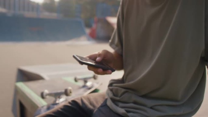 戴耳机的年轻人在滑板场使用手机
