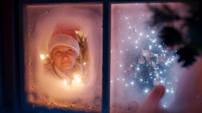 SLO MO幸福的女人在圣诞节之夜透过窗户看