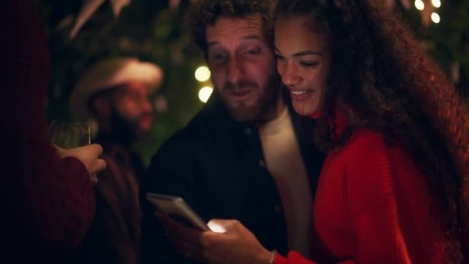 爱的混血夫妇在户外露台上使用智能手机或与朋友一起参加花园舞会。美丽的男人和女人看着电话亲吻，周末放松