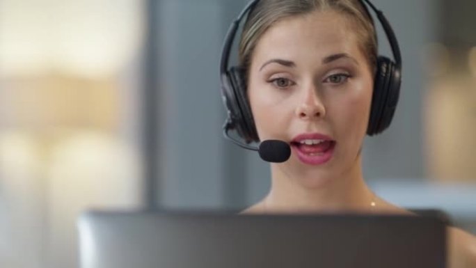 一个自信的年轻呼叫中心电话销售代理在办公室的笔记本电脑上进行虚拟视频通话时在耳机上交谈。友好的女性顾