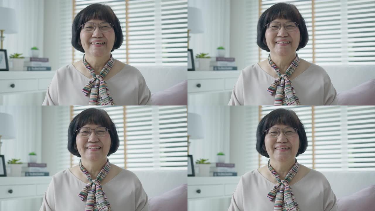 快乐的亚洲高级女性的肖像放松坐在沙发沙发上的家庭公寓微笑看着相机，享受退休或检疫的时光。迷人的亚洲成