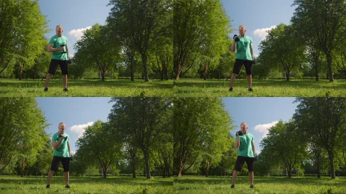 一个穿着绿松石t恤的金发健康男人在一个夏天的早晨在公园里用哑铃锻炼