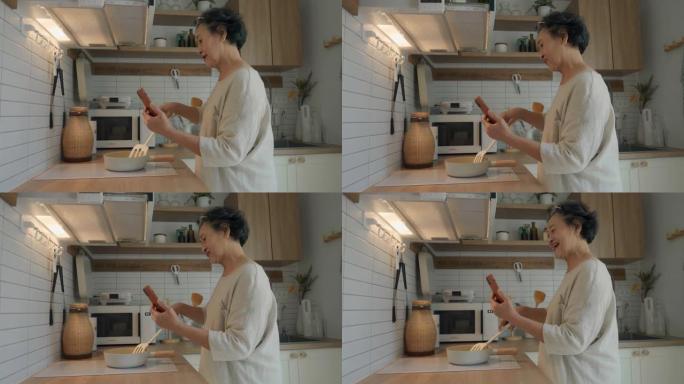 亚洲资深母亲在手机上聊天时在厨房做饭。