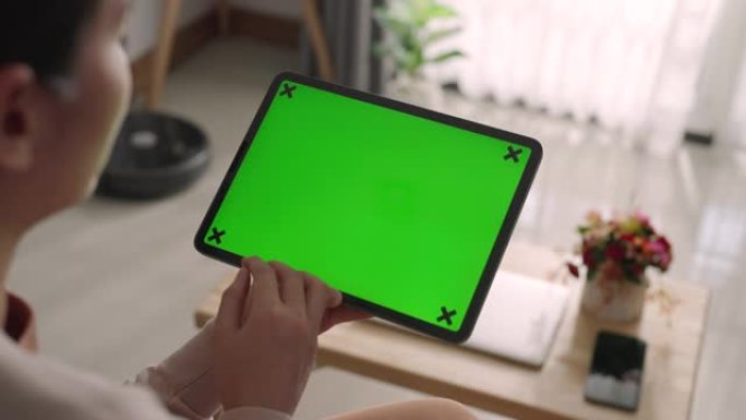 亚洲妇女在家中沙发上使用带有绿色屏幕的数字平板电脑