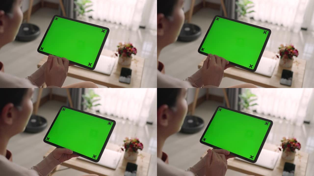 亚洲妇女在家中沙发上使用带有绿色屏幕的数字平板电脑