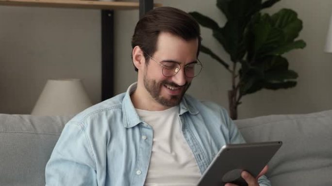 微笑着轻松无忧无虑的戴着眼镜的年轻人使用数字平板电脑。