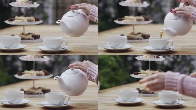 4k视频片段，一名妇女在外面的茶话会上将热茶倒入杯子中