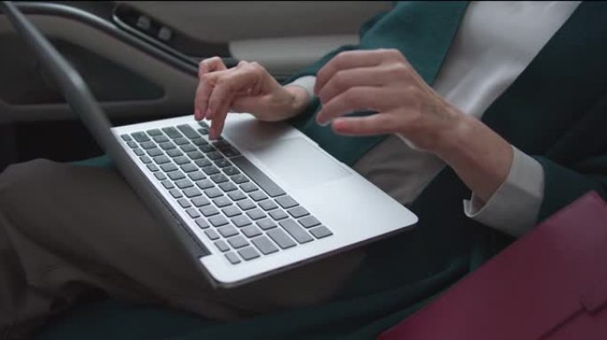 中年女性手的高角度视图，在笔记本电脑上打字，同时作为乘客乘坐汽车