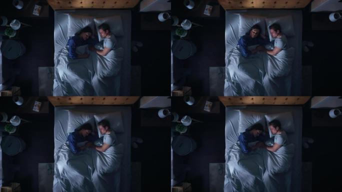 顶景公寓: 幸福的年轻夫妇晚上睡在床上。漂亮的女朋友和帅气的男朋友睡在一起。两口之家相向而睡。自上而