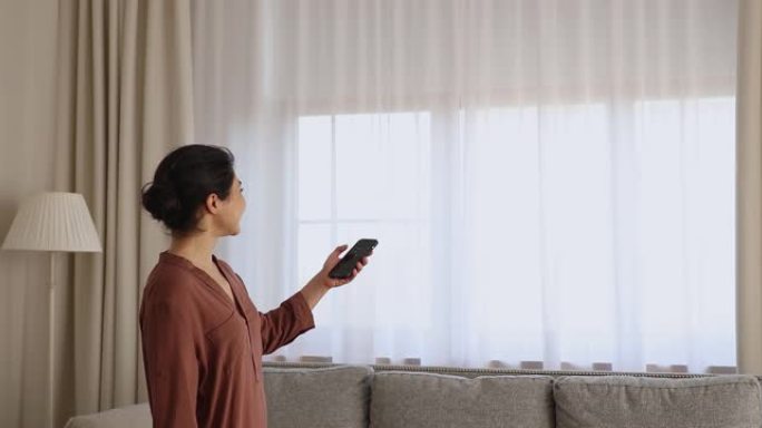 印度妇女关闭百叶窗室内手持手机使用智能家居应用