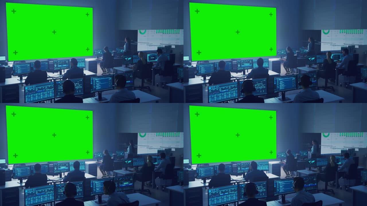 专业的计算机数据科学工程师团队在控制和监控室的台式机上工作。大显示屏有一个绿屏模型，其他显示图表、图