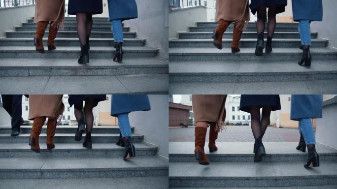 三个穿着秋天外套的快乐年轻女性朋友的后视腿在市中心的外面见面时走上楼。