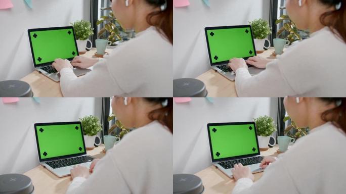 女人在家里的桌子上使用色度键屏幕笔记本电脑