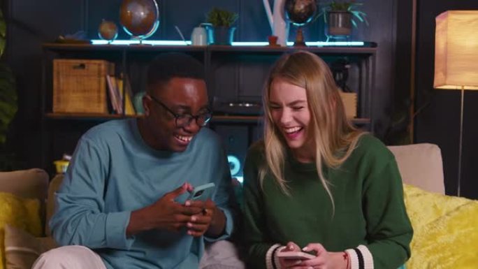 两个20多民族的快乐年轻朋友使用智能手机滚动互联网提要，在家里一起欢笑。