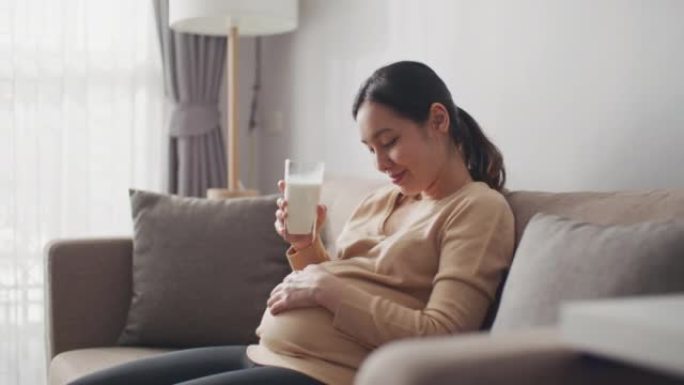 孕妇正在喝牛奶，轻轻地抚摸她的肚子