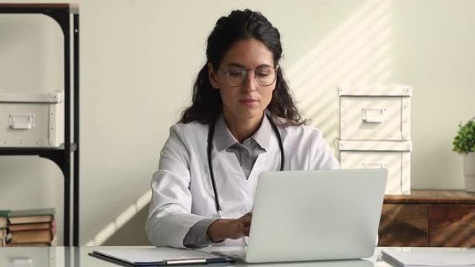 穿着白色制服的严肃女治疗师在笔记本电脑上工作