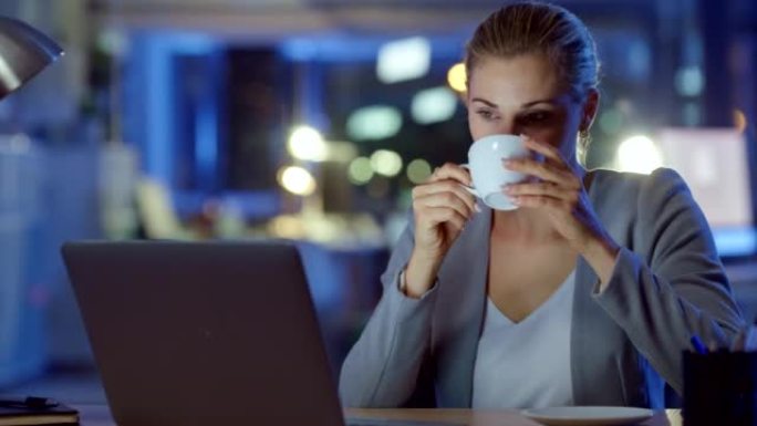 女商人一边喝咖啡，一边在笔记本电脑上阅读、键入电子邮件和在线财务报告。办公室经理工作到很晚，晚上在启