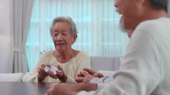 一群年龄在60-70岁之间的亚洲活跃老年人与一群快乐的老朋友在打牌的同时在疗养院度过了愉快的时光。社