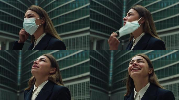 年轻的女商人脱下医用防护口罩，在摩天大楼的背景下深呼吸的电影特写镜头。企业概念，保护，病毒传输，安全